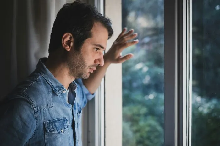 Pensive man looking out a window thoughtfully during difficult moments before deciding to choose divorce.