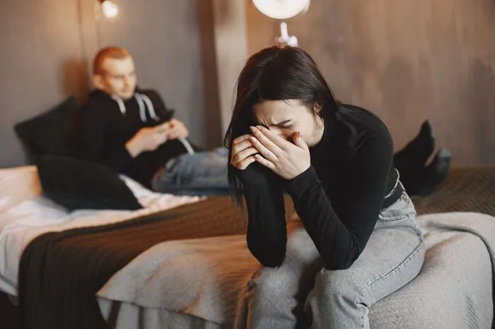 Distressed woman crying on a bed while her partner ignores her, a moment that makes one choose divorce.