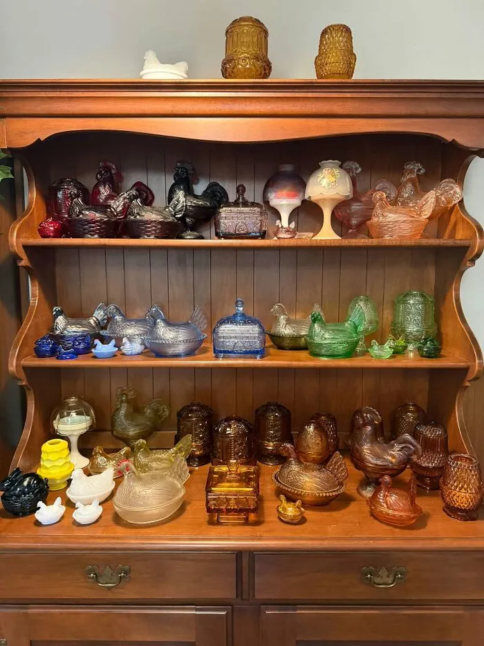 Collection of vintage glass hen-on-nest dishes in wooden hutch