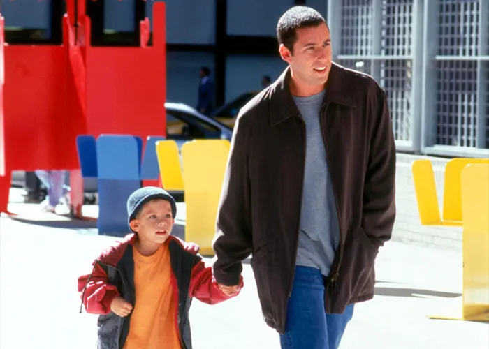 Adam Sandler holding hands with a young boy while walking outside