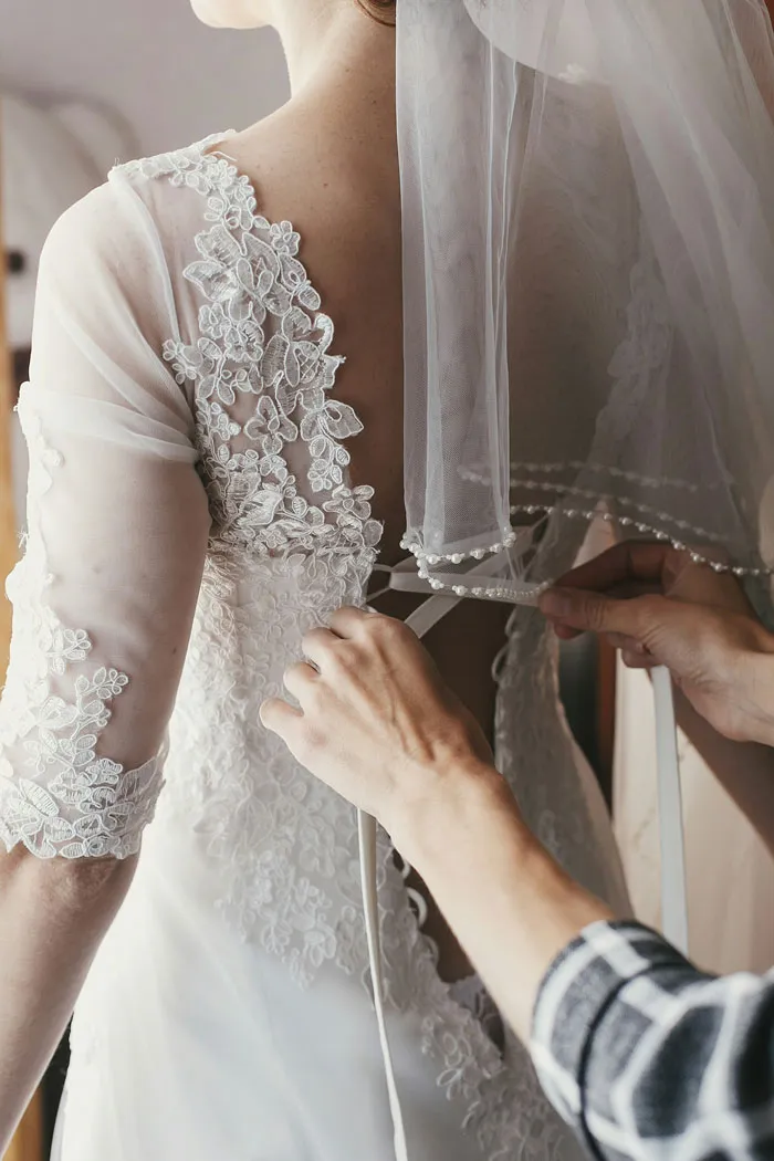 Bridesmaid helping bride adjust lace wedding gown connected to outrageous bridezilla stories.