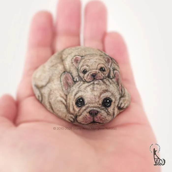 Hand holding stone painted with detailed dog and puppy art