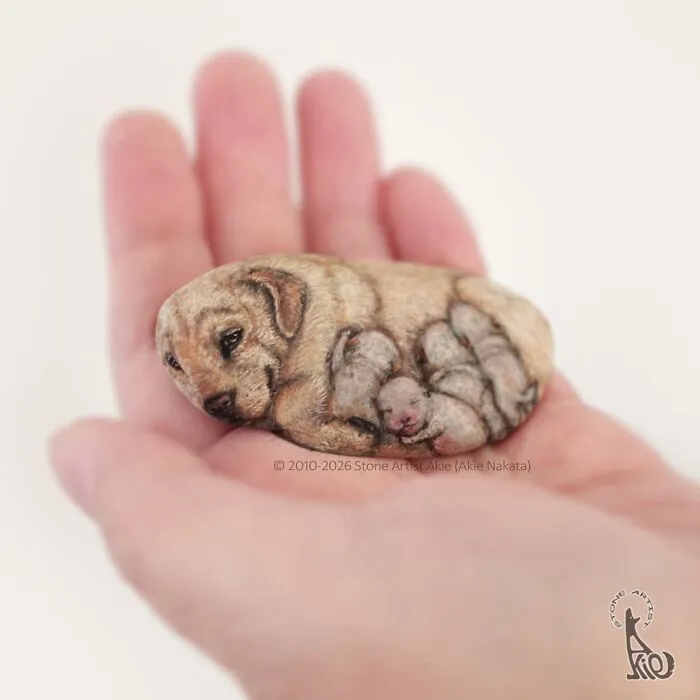 Realistic dog and puppies painted on a small stone in hand