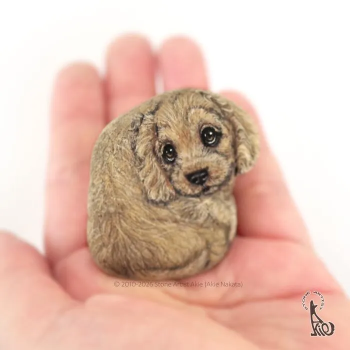 Hand holding stone with detailed painting of a cute dog face
