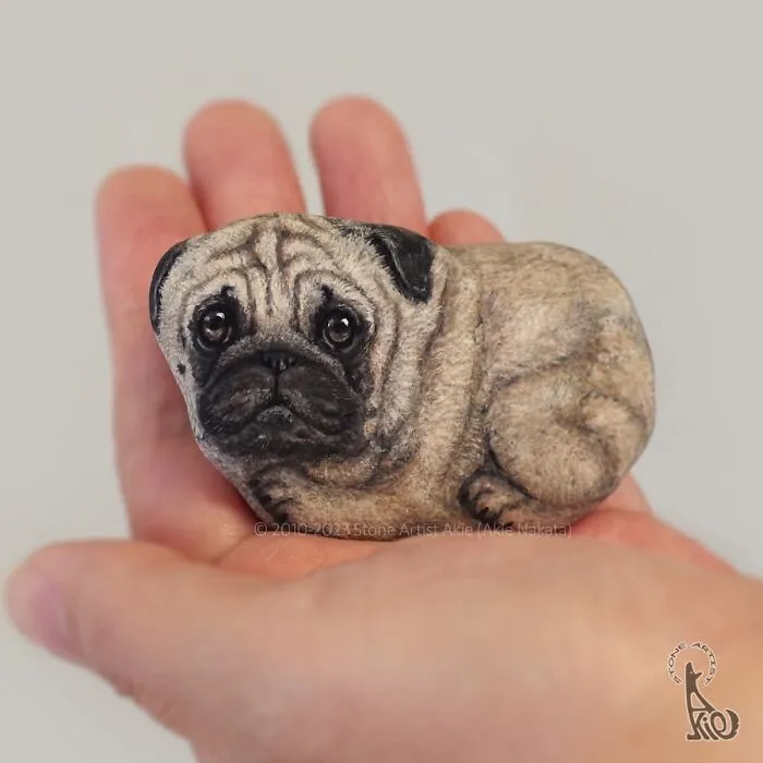 Hand holding stone painted as detailed pug dog by Japanese artist