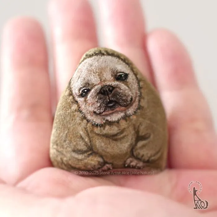Hand holding a stone painted with detailed dog face and body