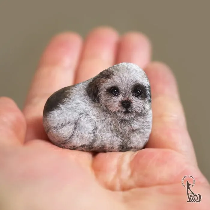 Small stone painted as a detailed cute dog puppy held in hand