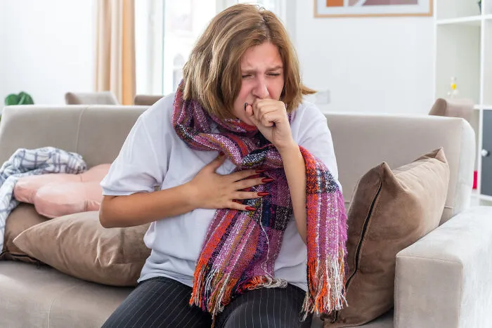A sick woman coughing on a couch, showing health issues leading to the choice to skip a second date.
