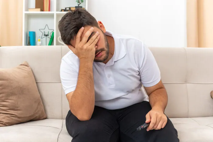 A stressed man covering his face on a couch, illustrating brutal stories of personal struggle.
