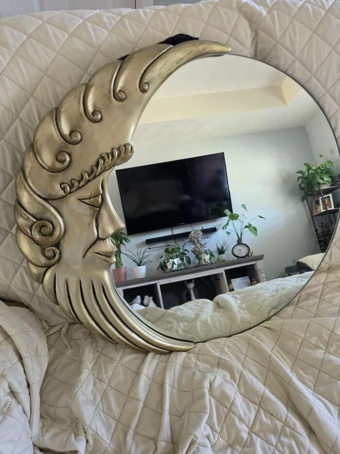 A gold crescent moon-shaped wall mirror reflecting a living room, highlighting cool thrift store finds.