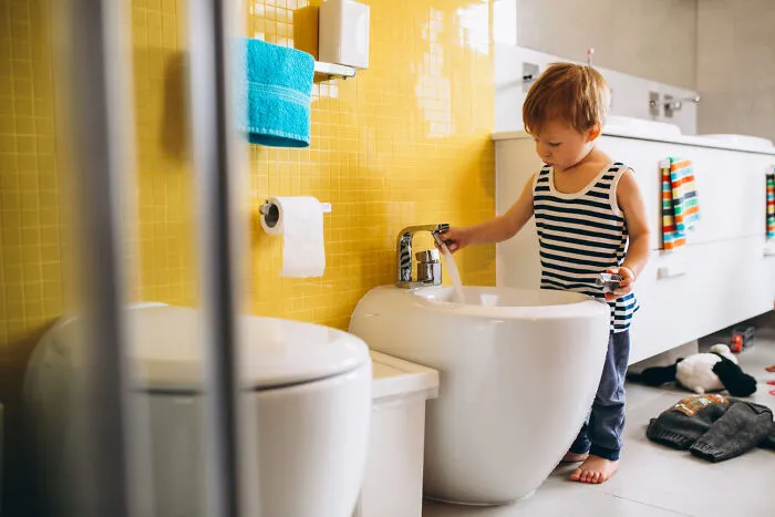 A young boy washing his hands at the bidet, exemplifying independent play versus helicopter parenting.
