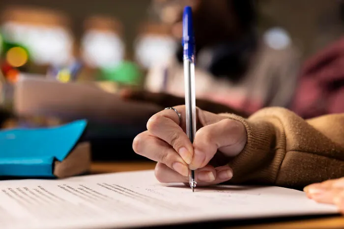 Close up of a student holding a pen and writing on a paper