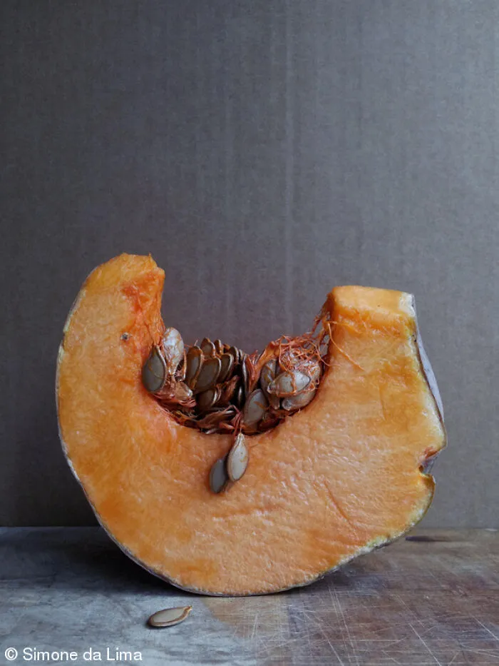 Fresh slice of orange pumpkin with seeds showing on a rustic surface.
