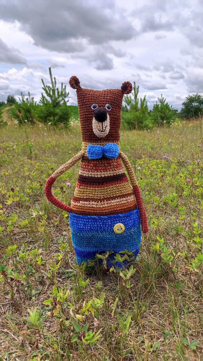 Cute brown bear crochet creature standing in grass field.