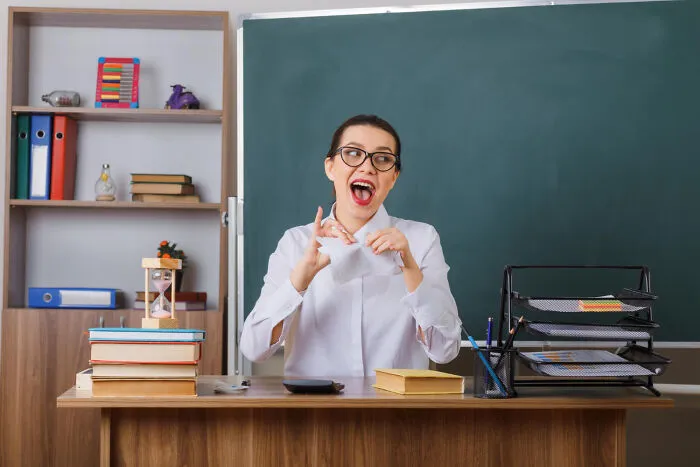 Angry teacher tearing up a piece of paper in front of a green chalkboard