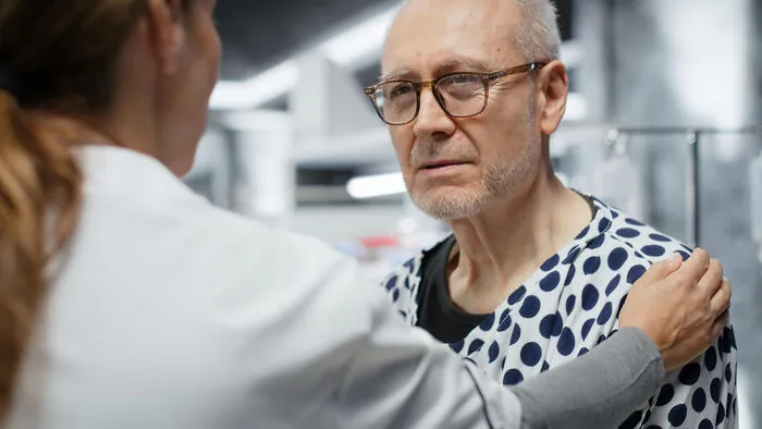 An older male patient receives comforting support from healthcare workers.