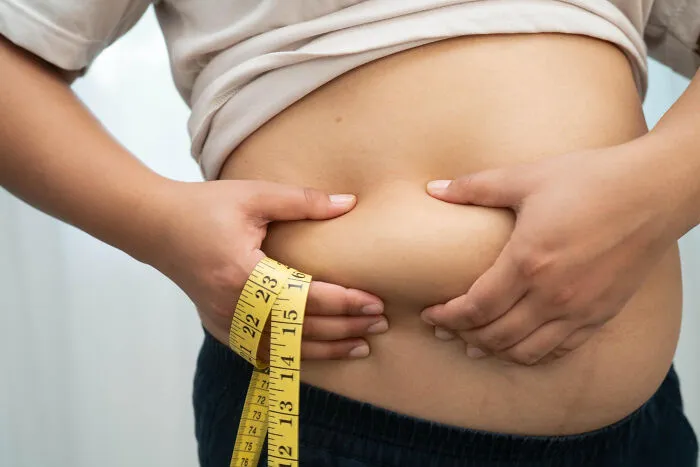 Person measuring waist with tape measure focusing on abdominal fat