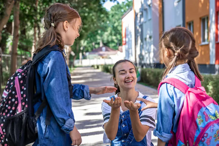 A smiling mother sending her young kids to school, discussing effects of helicopter parenting.