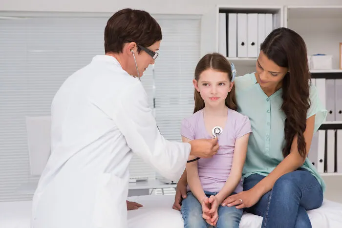 Doctor using stethoscope on young girl sitting with mother during checkup