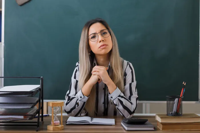 Serious teacher staring with disapproval in front of a chalkboard