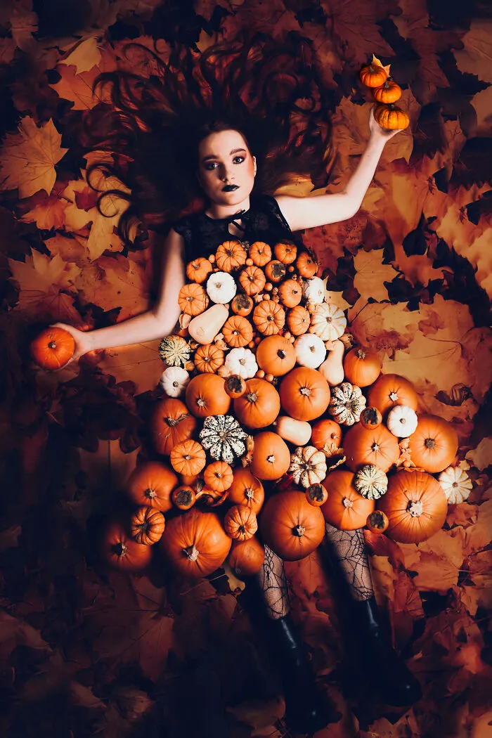 Woman wearing a dress made of miniature pumpkins lying dramatically on a bed of autumn leaves.