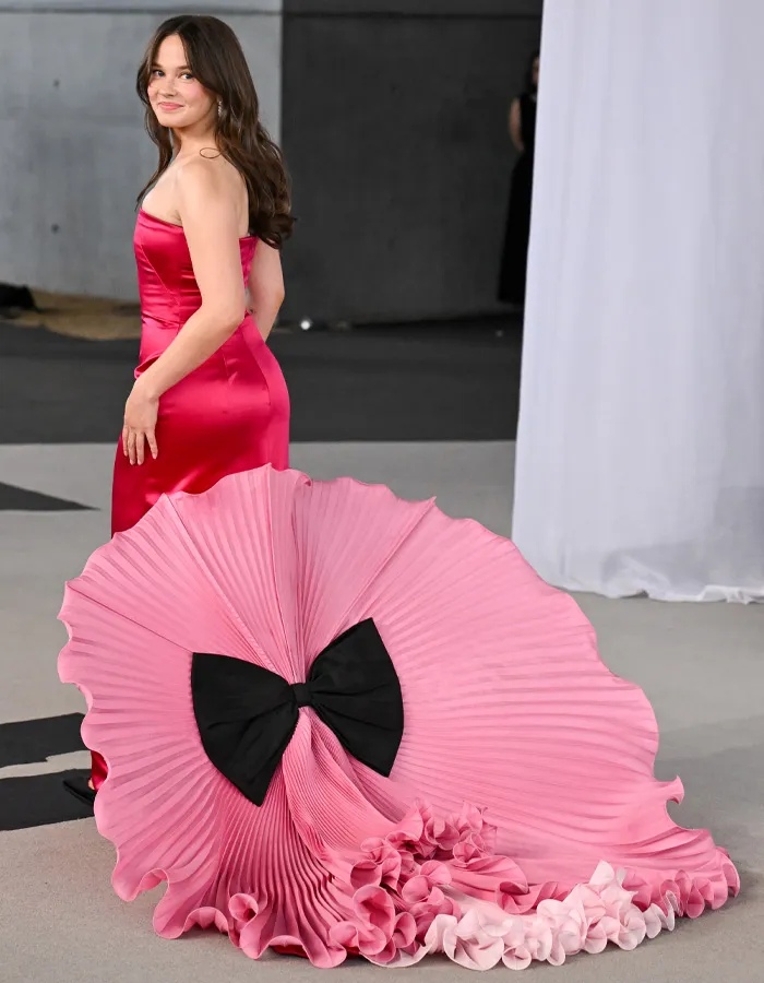 Woman in red satin dress with large pink fan detail at Academy Museum Gala