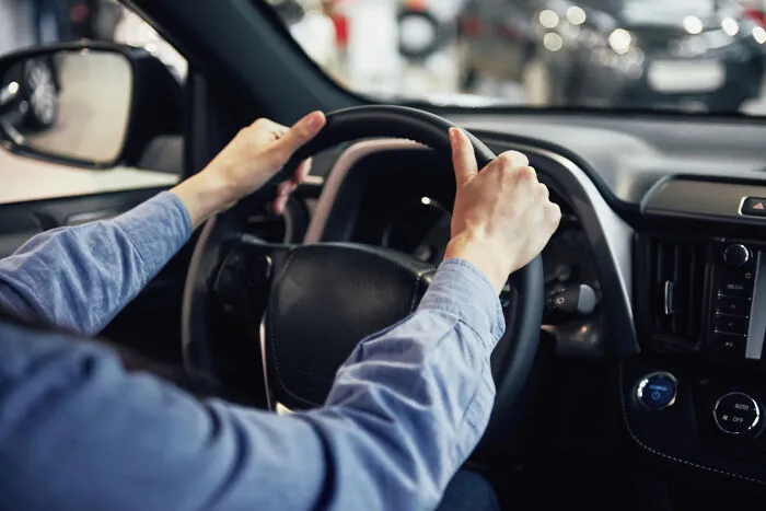 A driver holding the steering wheel inside a car, relevant to vehicle emergency tips.
