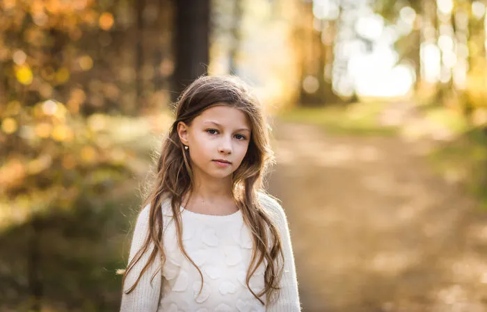 A young girl outdoors in a park looking cautious after encountering alarming words from strangers.
