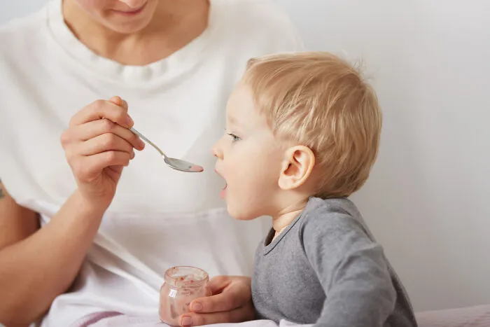 A mother spoon-feeding her toddler, representing overprotective helicopter parenting style.