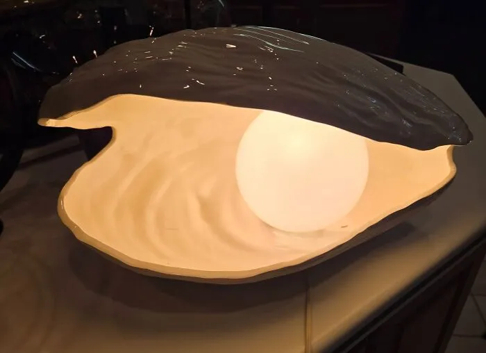 An open clam shell decorative lamp glowing softly inside, a unique thrift find displaying a lighted pearl design.