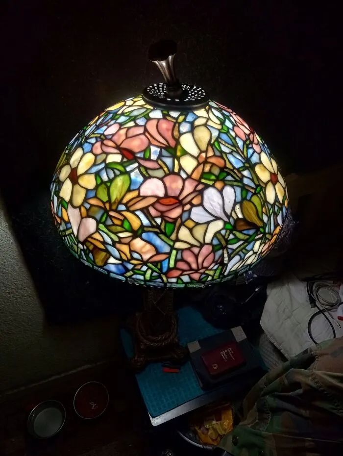 A colorful floral stained glass lamp shade glowing warmly, showcased among thrift finds.