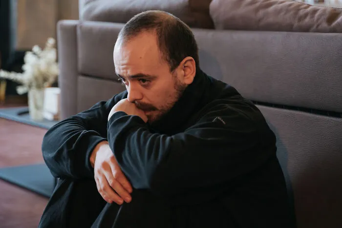 A sad man sitting alone on the floor, thinking about how his lifelong friendships fizzled out.