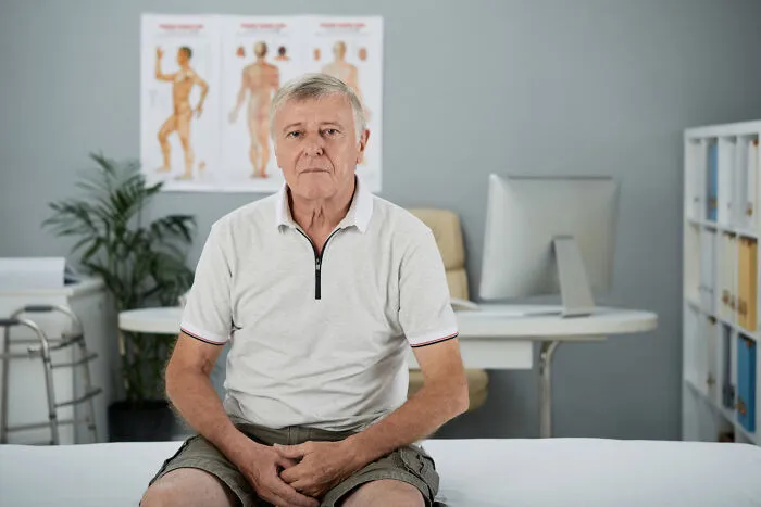 An older male patient sits on an examination table in a healthcare clinic.