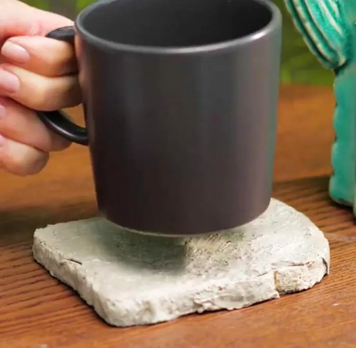 A black mug being placed on a rough, bread-shaped stone coaster from DIY projects.