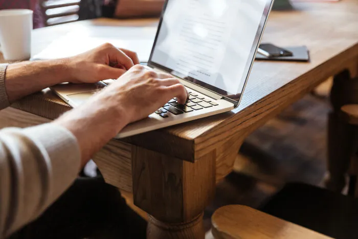 Person typing on a laptop computer keyboard at a wooden desk with obvious lies.