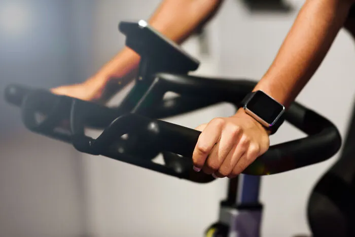 A person riding a stationary exercise bike with a smartwatch, showing obvious lies about fitness routines.