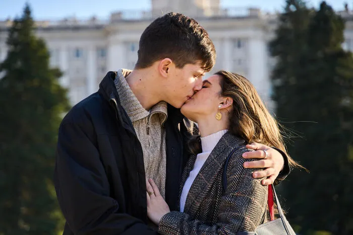 Young couple sharing a kiss outdoors in front of building