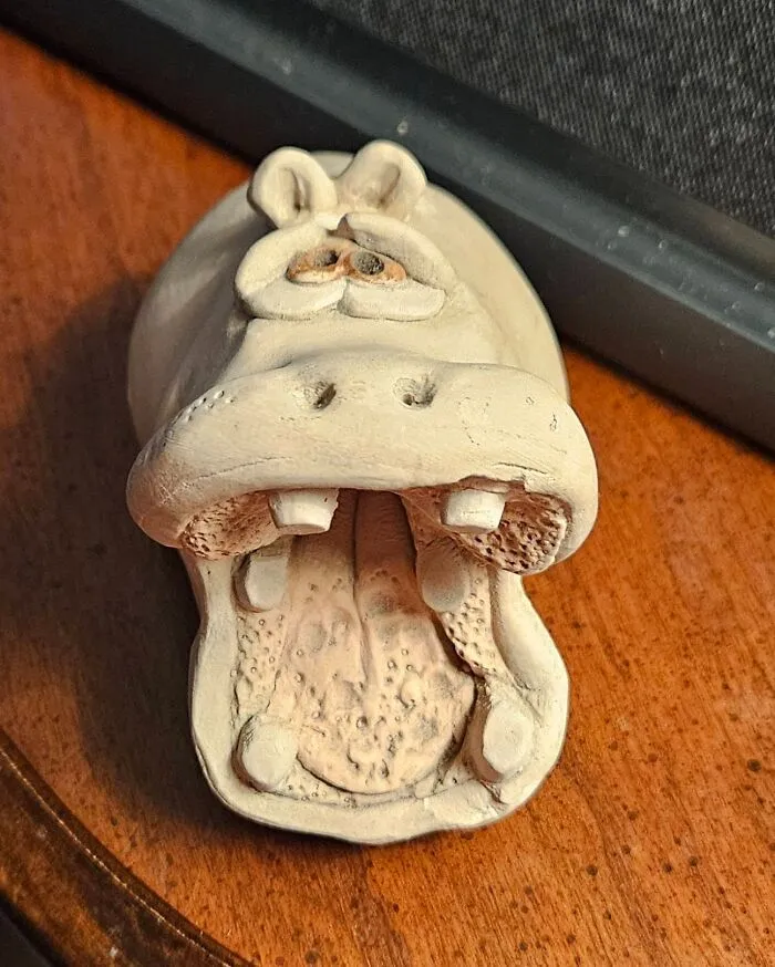 An open-mouthed clay hippopotamus sculpture sitting on a wooden surface as a unique thrift find.