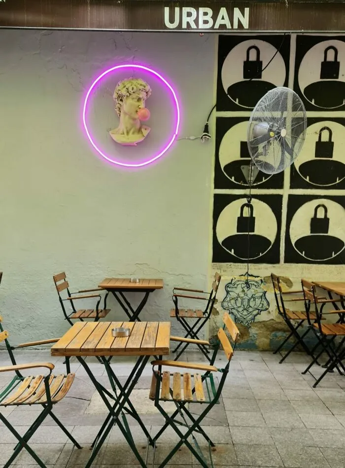 A neon pink circular light surrounding a sculpture bust of David on a city streets cafe wall