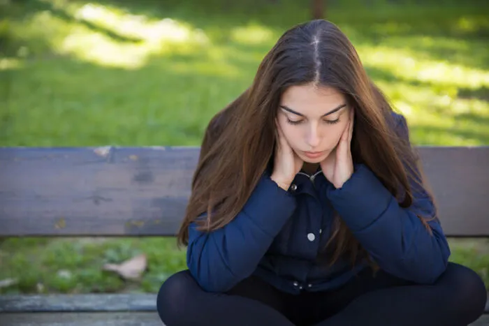 Stressed young woman on a bench, affected by helicopter parenting