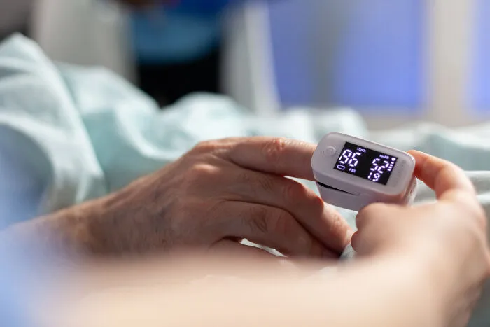 Healthcare workers using a pulse oximeter on a patient's finger to check oxygen levels.