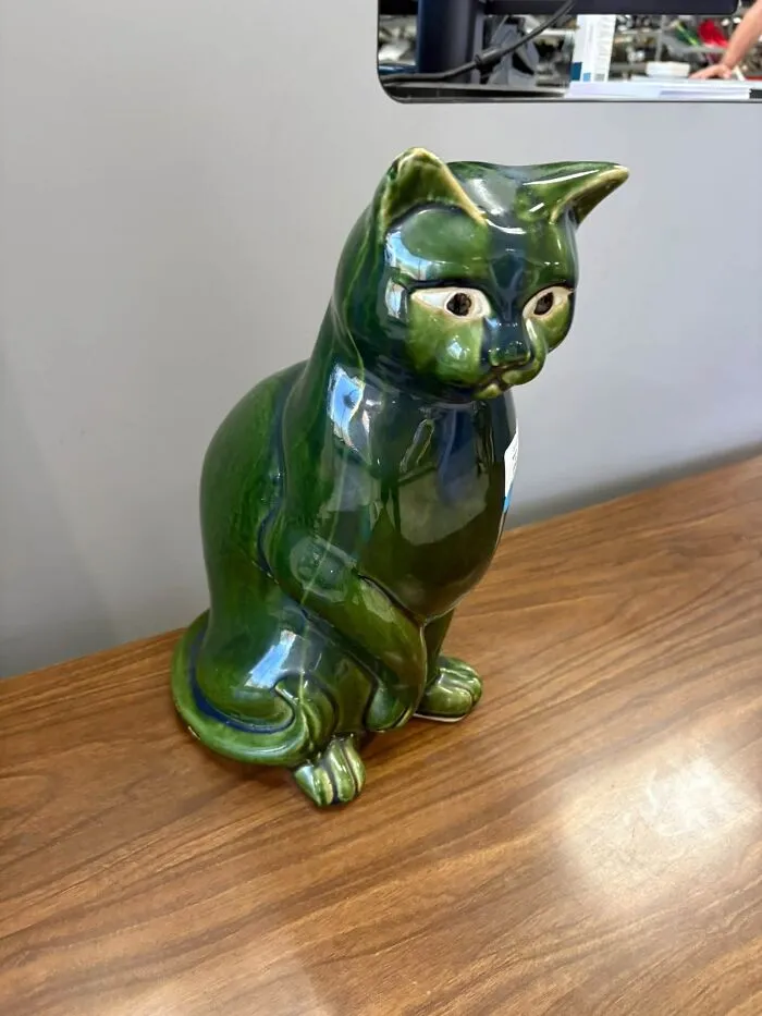 A glossy green ceramic cat statue displayed on a wooden surface as unique thrift finds.