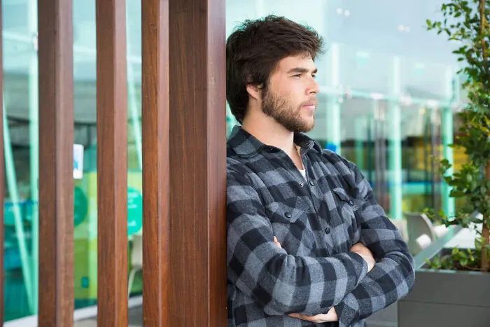 Pensive man leaning against a wooden pillar contemplating if he should skip a second date