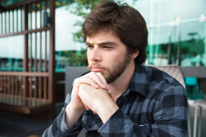 A pensive young man sitting outside, contemplating the reasons why lifelong friendships fizzled out.