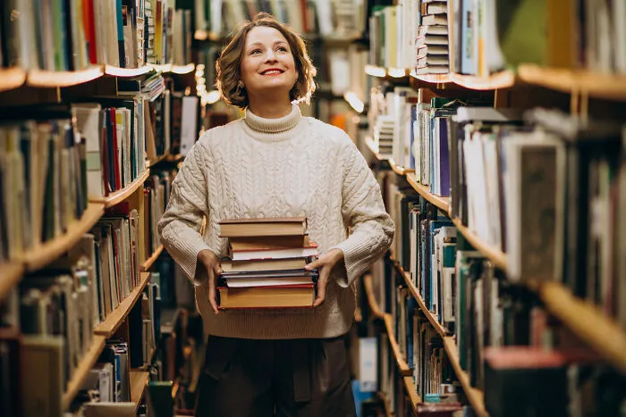 A happy woman holding a stack of books in a library, representing a quiet setting where strangers said unexpected things
