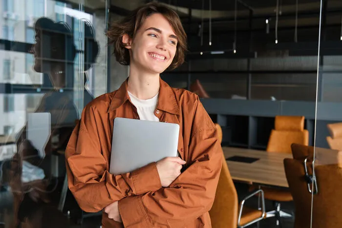 Smiling young woman holding laptop in modern office space
