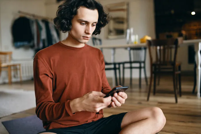 A young man looking at his phone with a serious expression as lifelong friendships fizzled out.