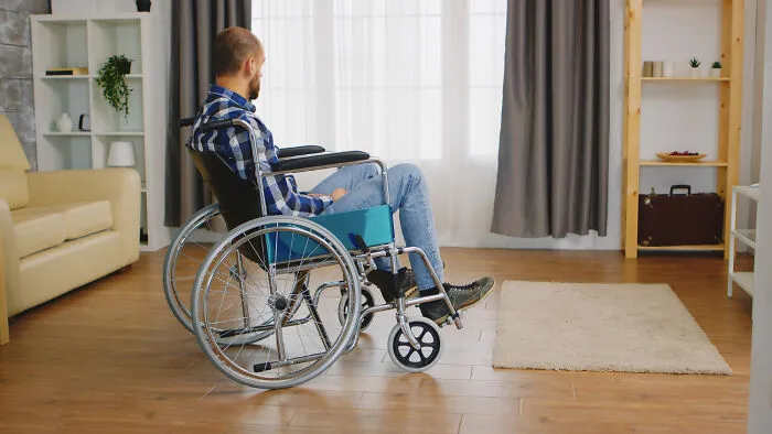 A man in a wheelchair looking out a window, experiencing the loneliness of fizzled out friendships.