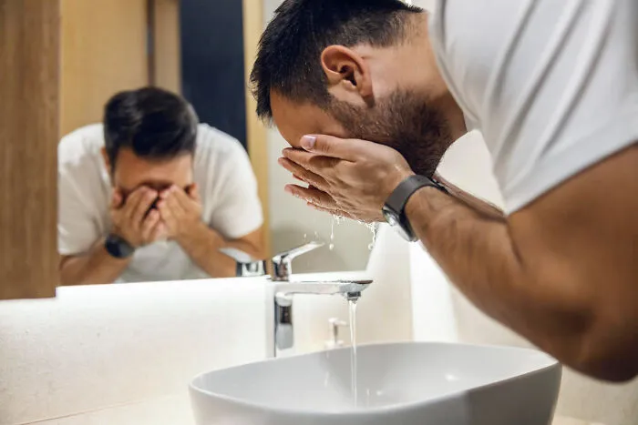 A man washing his face in a bathroom mirror, representing candid thoughts doctors and nurses have about hygiene