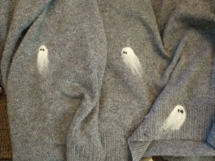 Cute needle-felted ghosts embroidered on a grey sweater, proving creativity can save money.